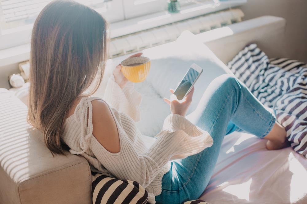 girl sitting on couch with cup of coffee looking at phone